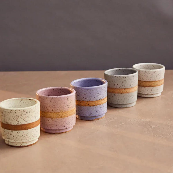 Set of five ceramic cups with striped designs on a brown surface and gray background