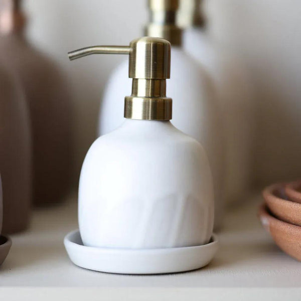 White soap dispenser with gold pump on a white surface