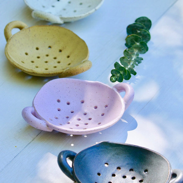 Four ceramic colanders in different colors on a light blue background