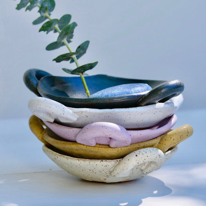 Stack of colorful ceramic bowls with a plant on a light background