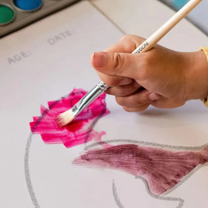 Hand holding a paintbrush over a piece of paper with pink paint and a fish outline.