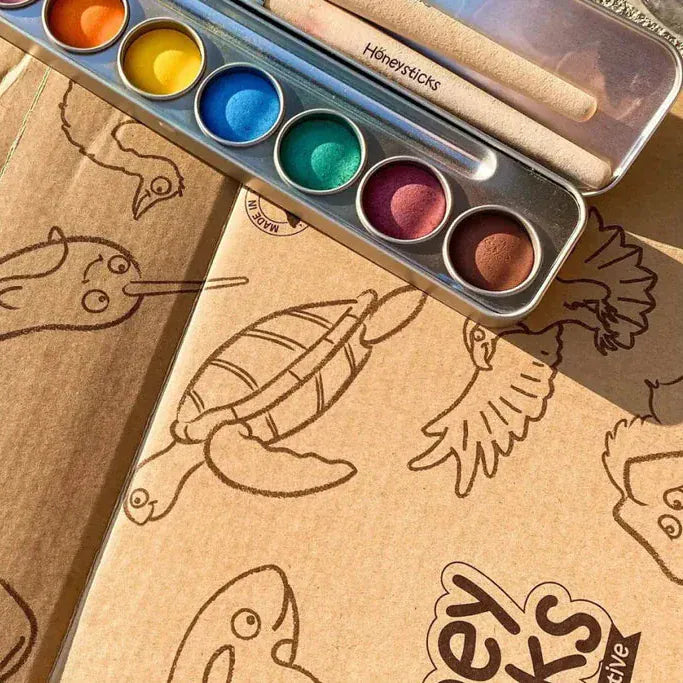 Coloring book with animal illustrations and a set of watercolor paints on a wooden surface.